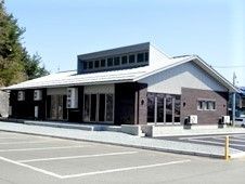 体育館のような形をした建物の外観写真。手前にある駐車場スペースも映っている