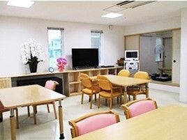 ピンクの椅子がセットされたダイニングテーブルが複数置かれた食堂には花が飾られ、カラオケセットやテレビもある。