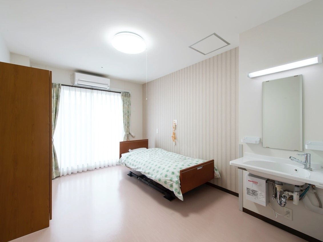 緊急通報装置が付いたフローリングの部屋には寝具付きのベッドが置かれ、エアコンも付いている。