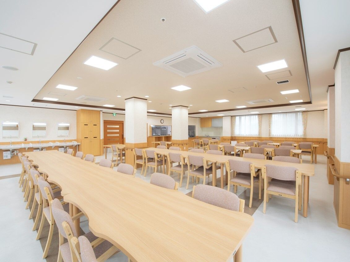 木製のテーブルセットが多く設置された食堂。左奥には車いす対応の洗面所が付いている。