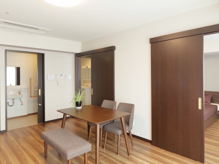奥に水回りがある2部屋タイプの部屋の写真。テーブルと椅子が並んでいる窓辺