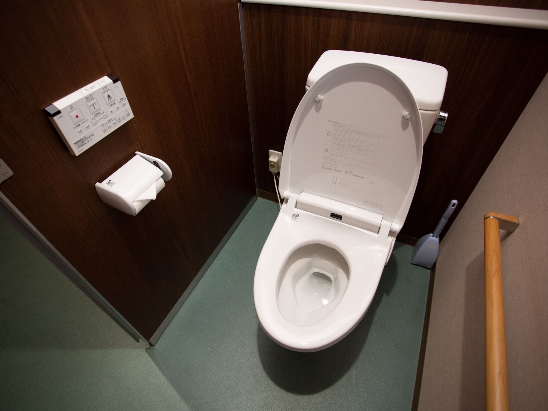 トイレはバリアフリーになっている。壁には、手すりと温水洗浄便座のリモコンが設置されている。トイレブラシが置かれている。