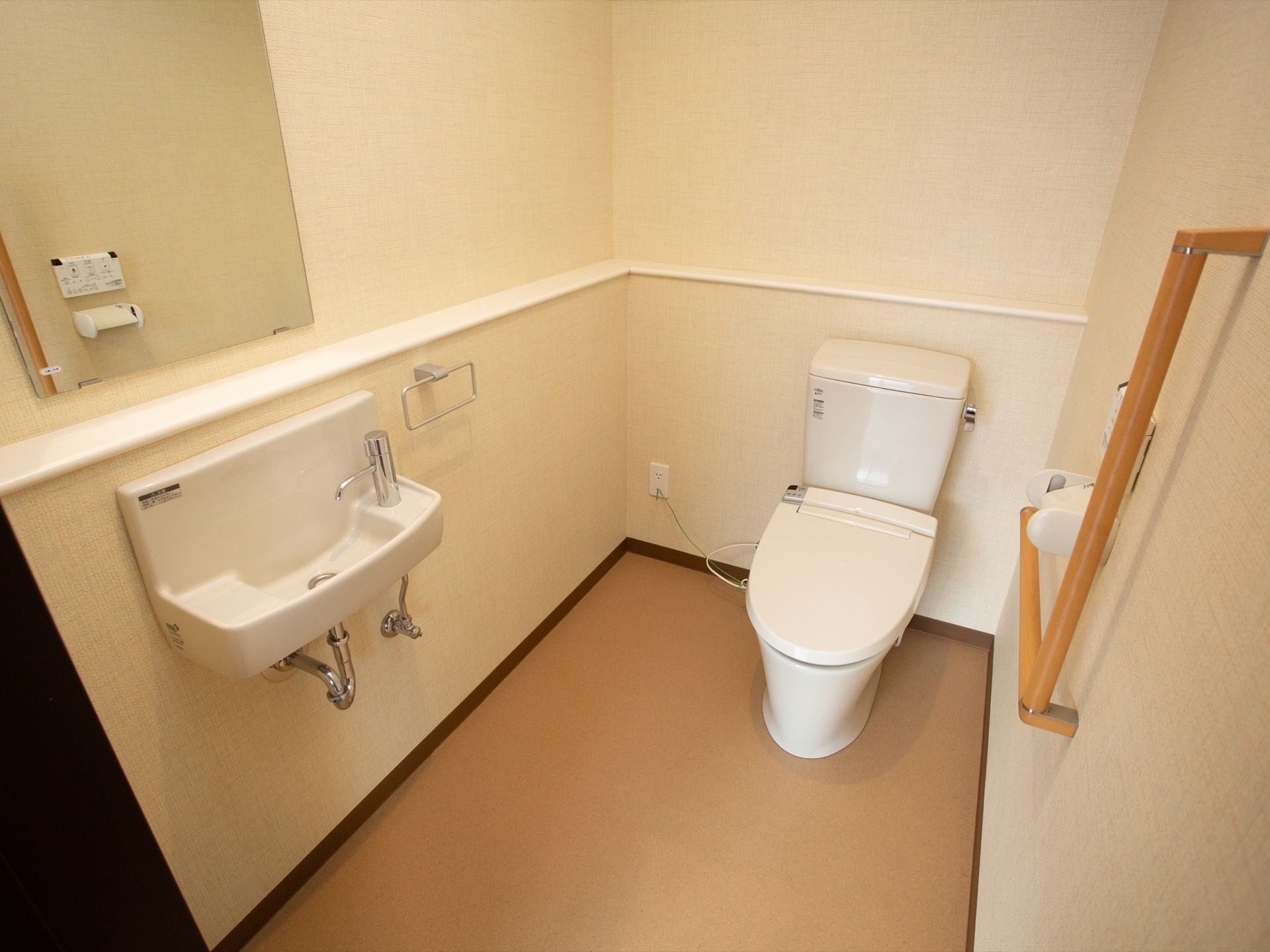 居室のトイレである。広めのスペースを確保しており、L型手すりや洗面台、温水洗浄便座が完備されている。