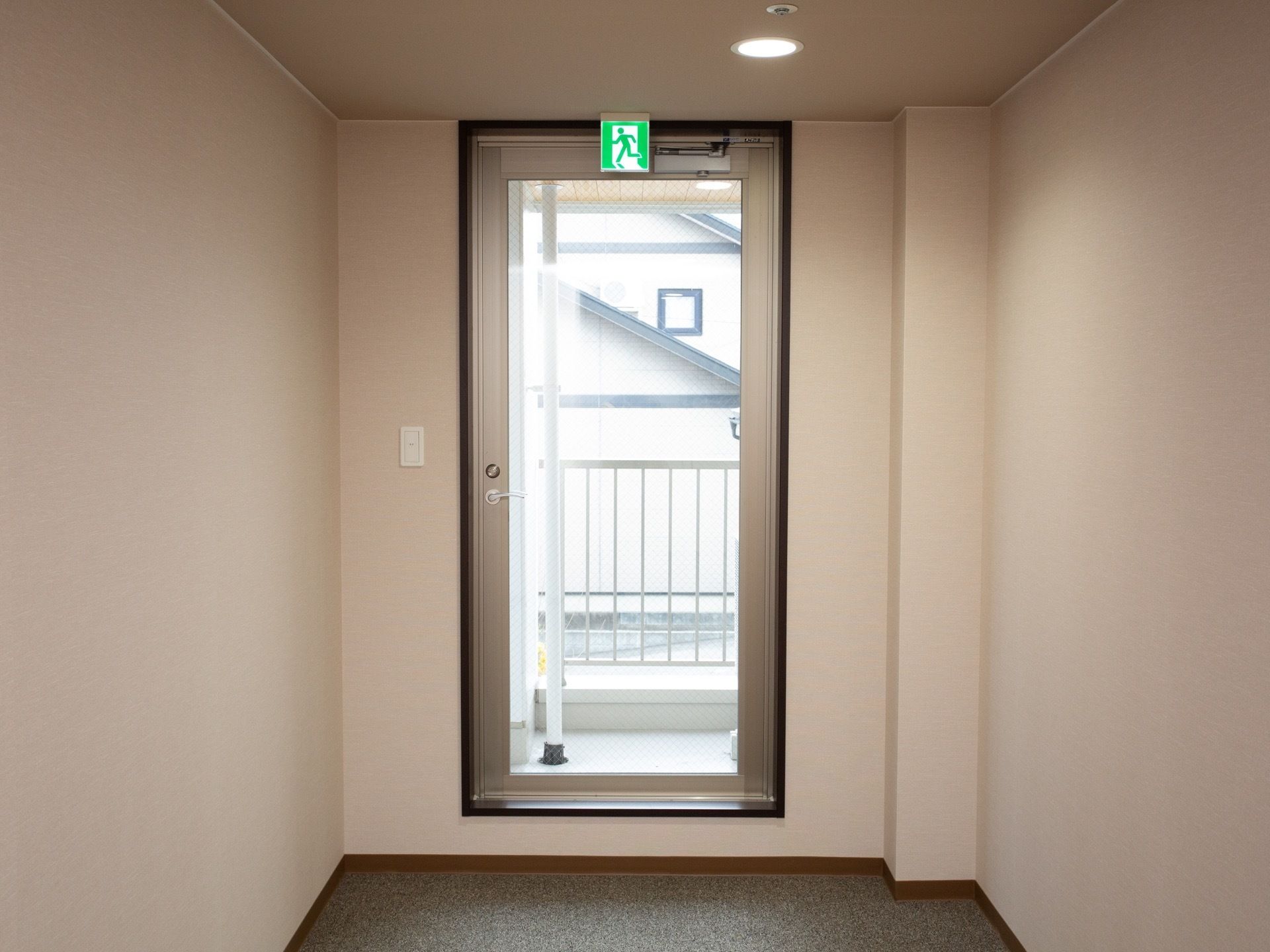 廊下には、非常口が設置されている。非常口からは日の光が差し込んでいる。床はカーペットが敷かれている。
