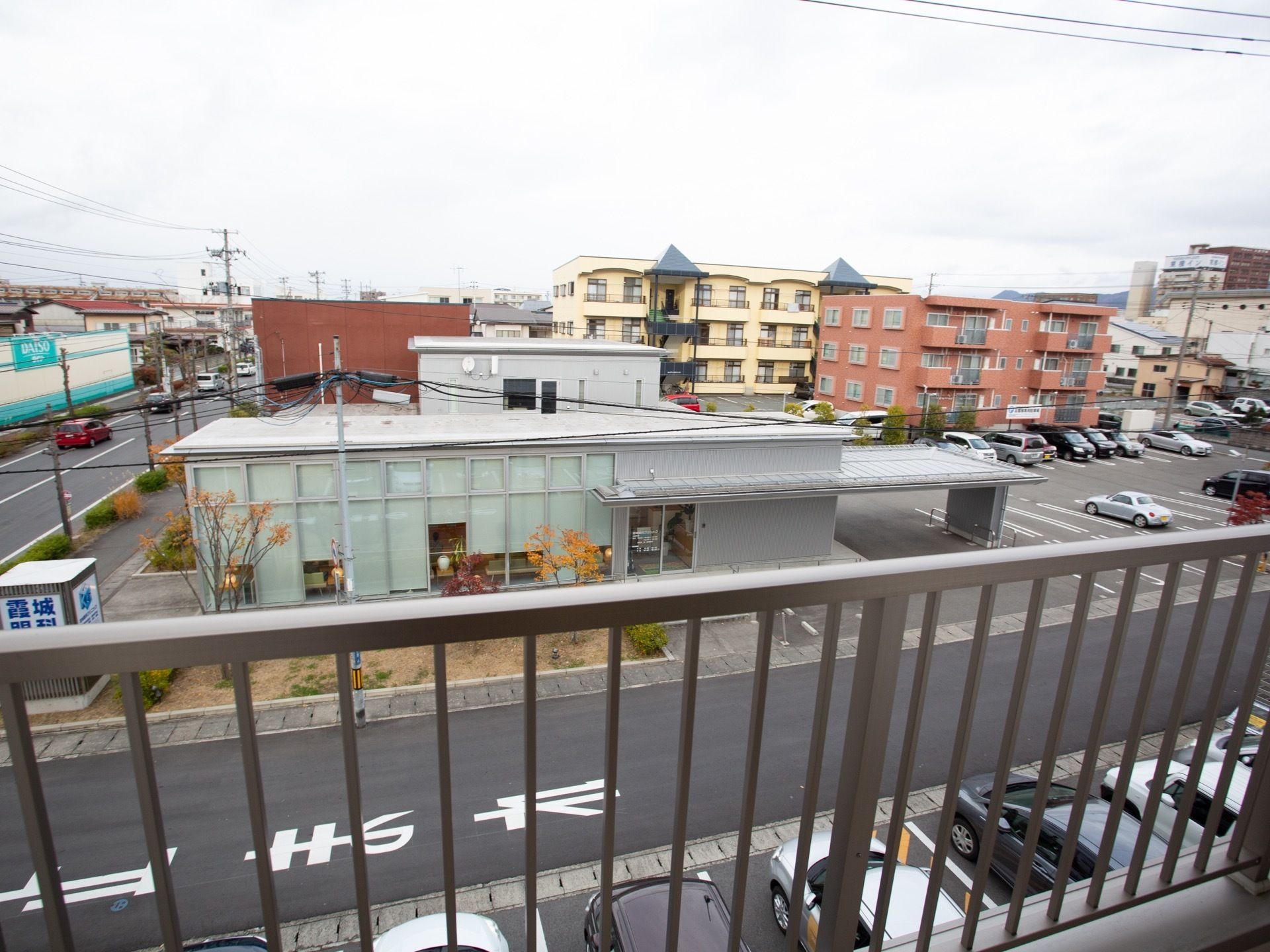 ベランダからは住宅街を一望することができる。遠くには山を望むことができる。敷地内には車が何台も停められている。