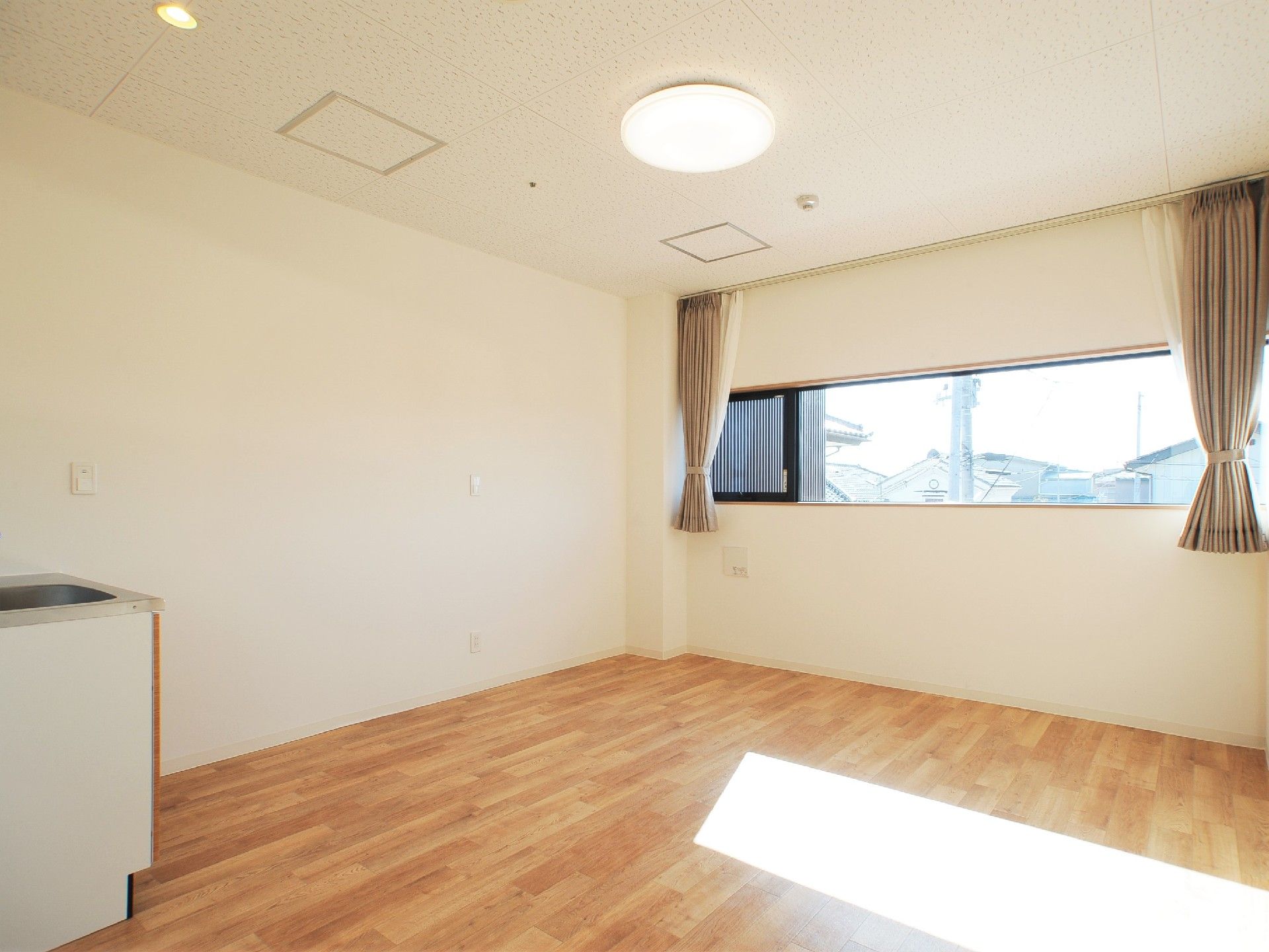 大きな窓にカーテンがついたフローリングの居室にはキッチンも付いている。