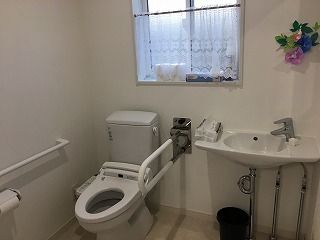 花が飾られたトイレは広く、ふたのない便座が設置されている。手すりが両サイドについている。