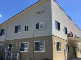 1階部分がベージュ、2階部分が白い２階建ての建物。外壁に住宅名がカラフルな文字で書かれている。