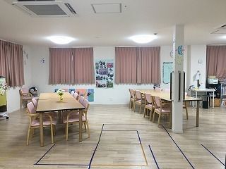 ピンクのカーテンが付いた窓がある食堂には木製のダイニングテーブルが並び、手作りの飾りも飾られている。