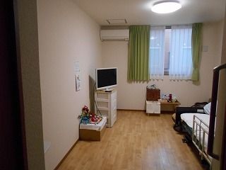 テレビやエアコン、寝具付きのベッドなどが置かれたフローリングの部屋にはカーテン付きの窓もある。