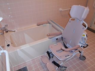 車いすタイプのリフトが設置された浴室。一人用の浴槽にはレールが付き、壁には手すりが付いている。