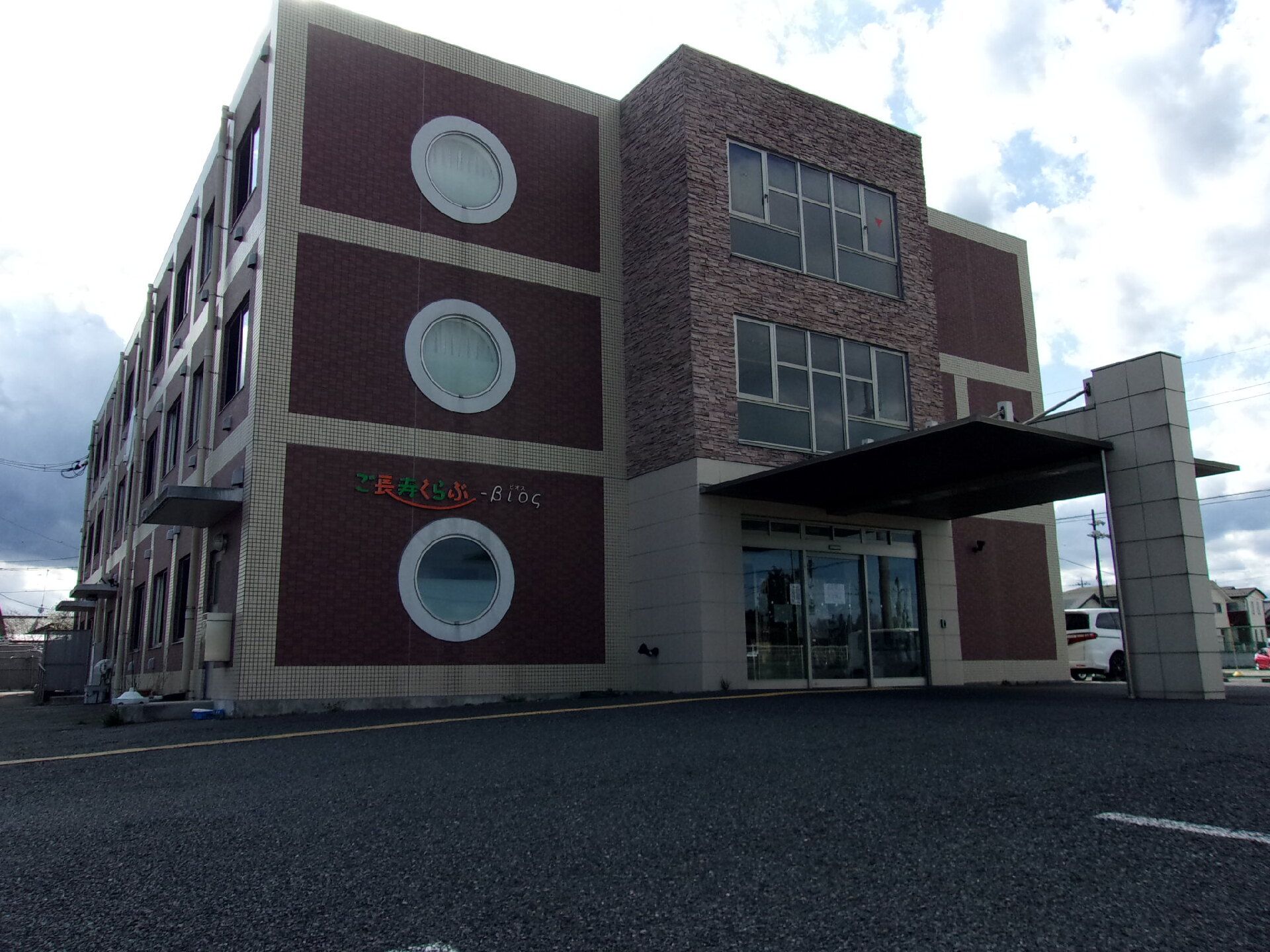 3階建てのブラウン系の建物には円形の窓が複数付き、住宅名が外壁に書かれている。