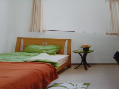 カーテンが付いた大きな窓が付いた明るい部屋には寝具付きのベッドが置かれ、テーブルもベッドサイドにある。