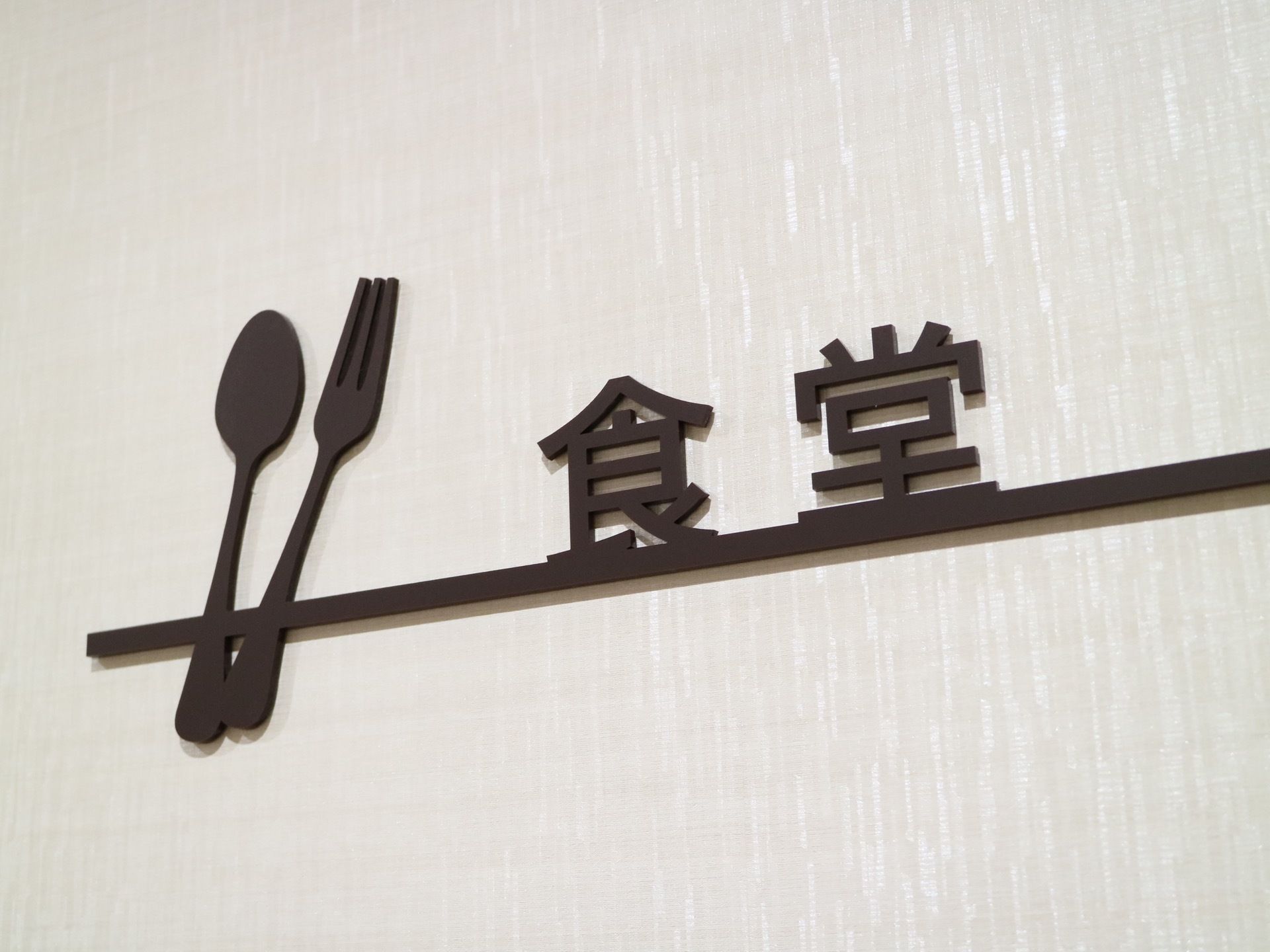 食堂の案内板が壁に取り付けられている。食堂内の家具と同じブラウンで、設備名とともに食器がデザインされている。