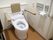 背もたれと可動式の手すりの備わったトイレである。壁にはナースコールや自動洗浄器の操作ボタンが付いている。