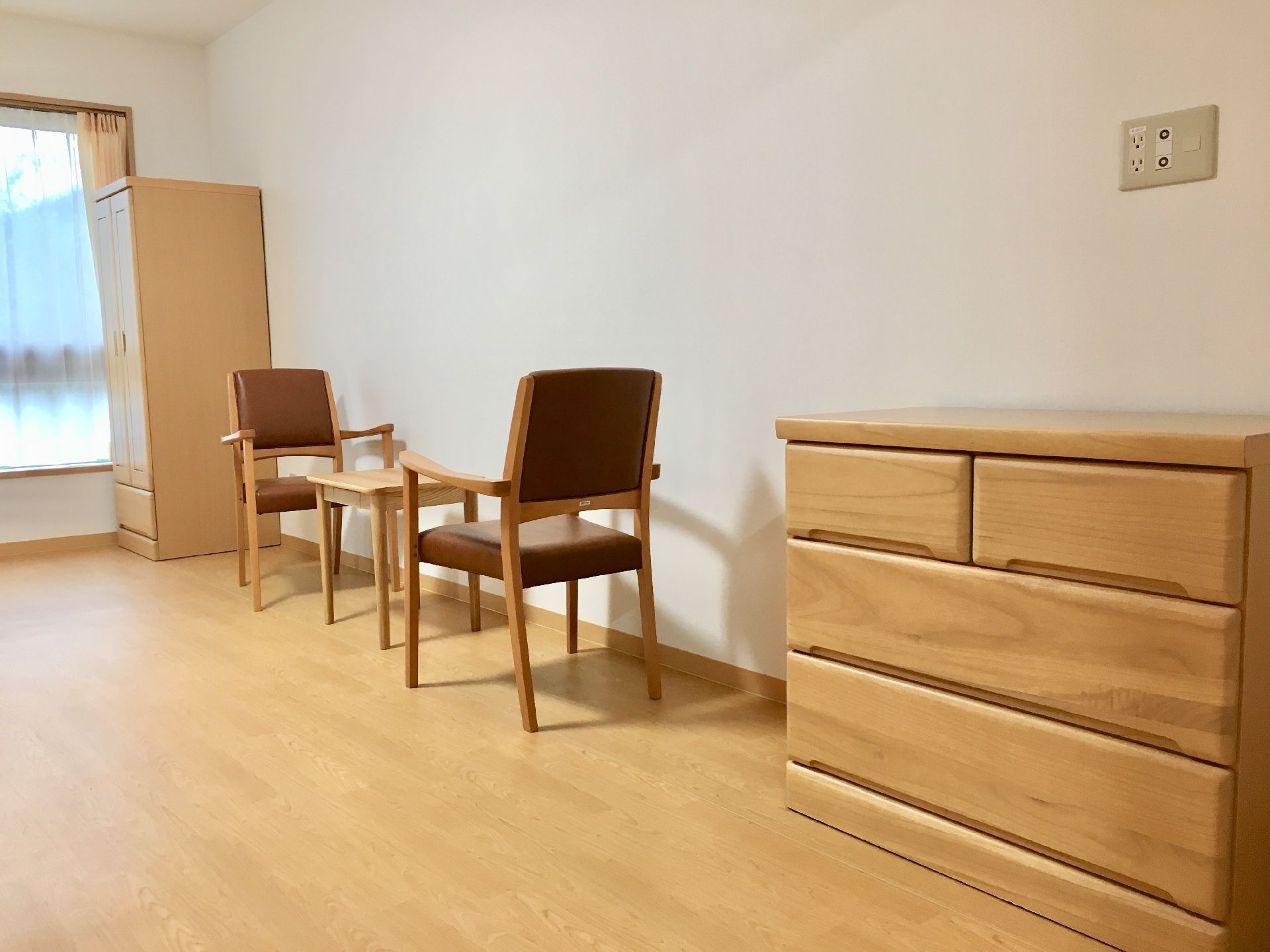 明るい色調の木製の家具が置かれている、大きな窓がある居住スペース