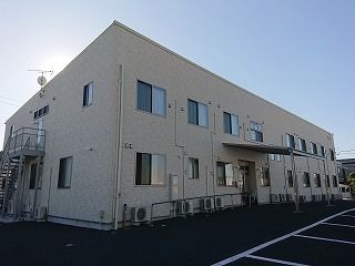 横に長いライトグレーの2階建ての建物は玄関には大きな屋根があり、手すり付きのスロープもある。