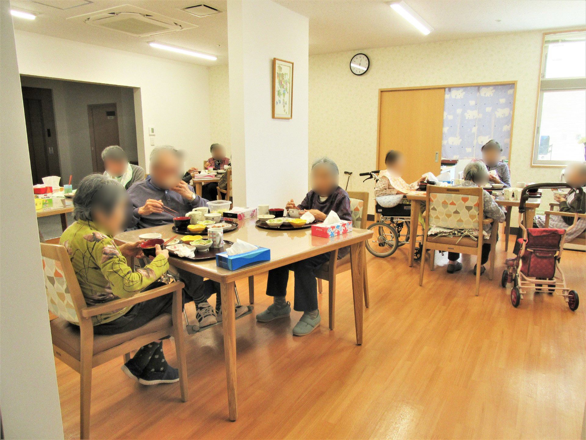 多くの高齢者が集まって食事をとっている様子。施設内のリビングの食事風景