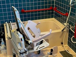 赤い手すりが設置された浴室にはレールが付いた浴槽や車いすタイプのリフトがある。