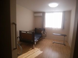カーテン付きの大きな窓があるフローリングの部屋にはベッドやテーブル、エアコンなどが設置されている。