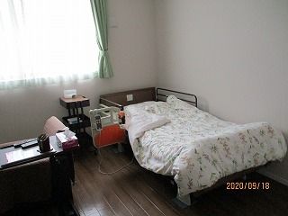 花柄の寝具付きのベッドやいすなどが置かれたフローリングの部屋には、レースカーテンとカーテンが付いた大きな窓がある。