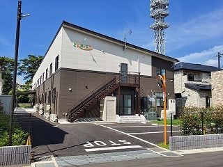 白とブラウン２階建ての建物は日当たりもよく、敷地内には駐車スペースもあり、緑も周りにある。