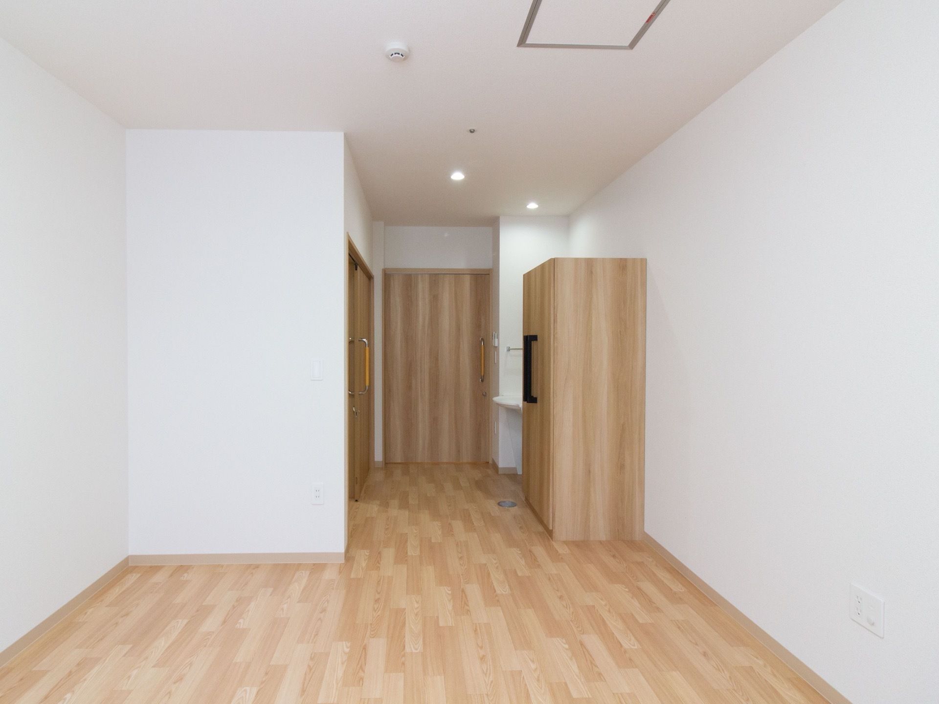 居室の床やドア、収納が木目調になっていて、壁は白い。天井には火災報知器や、丸い小さな照明が設備されている。