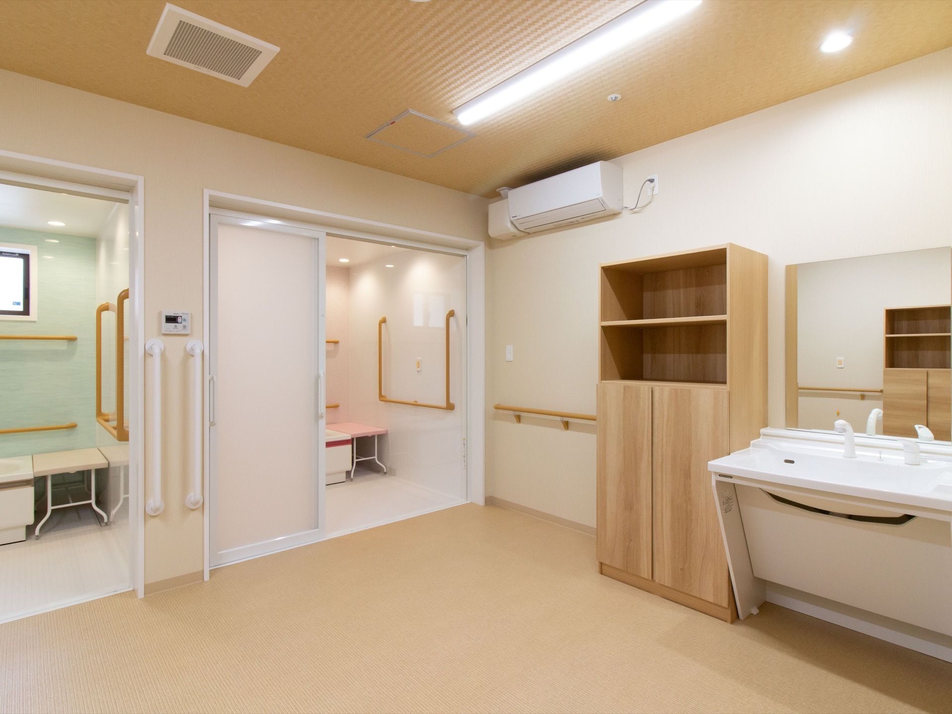 壁際に洗面台と木目調の棚が設置されている脱衣所。隣には浴室が2カ所あり、すりガラスの引き戸がついている。