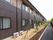 建物に沿って花壇や歩道が設けられている。建物の横にはエアコンの室外機が設置されていて、近くには苗木が植えられている。