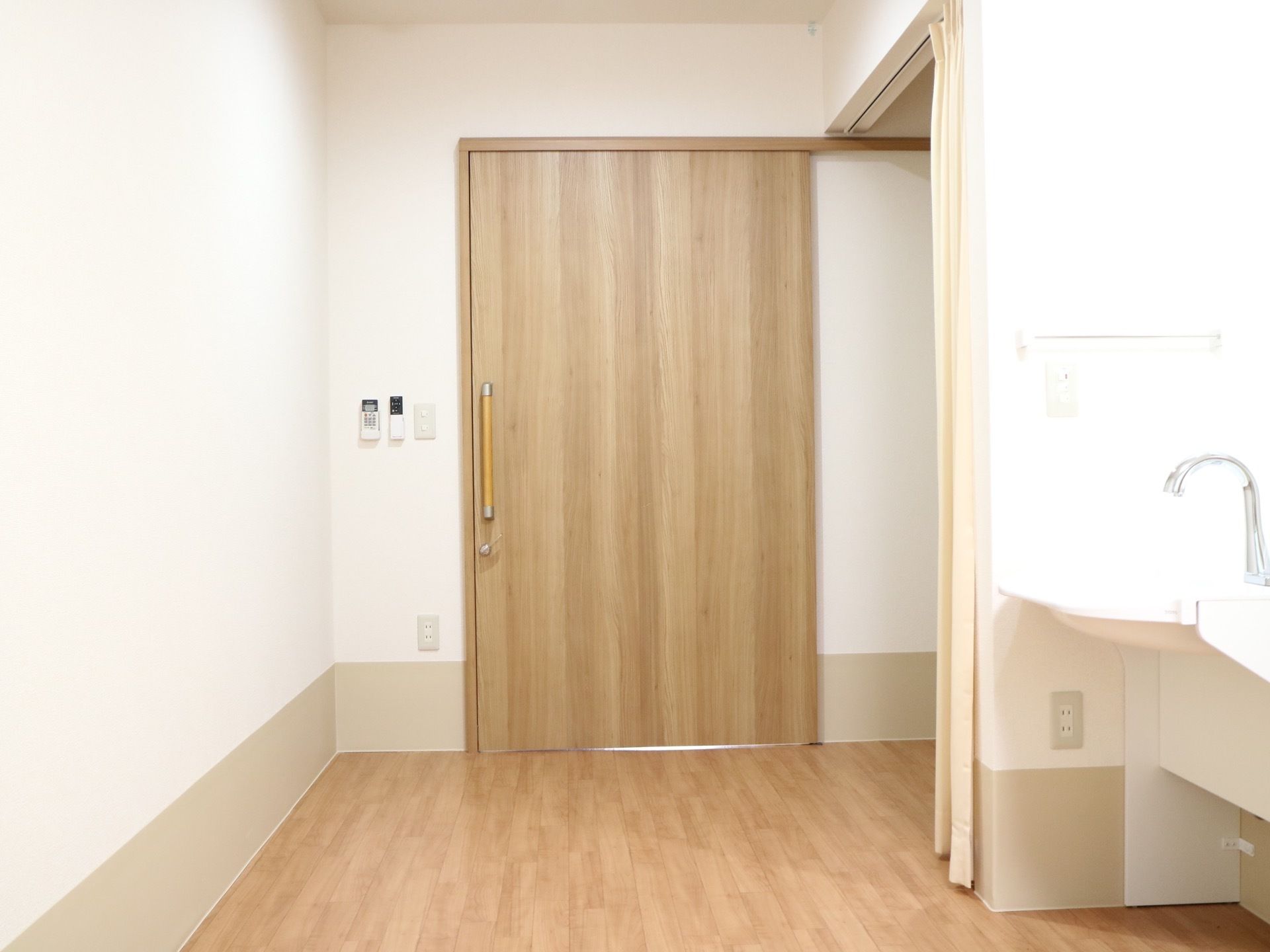木目調の大きな引き戸で仕切られた、フローリングの居室がある。壁際には照明付きの洗面台が設置されている。