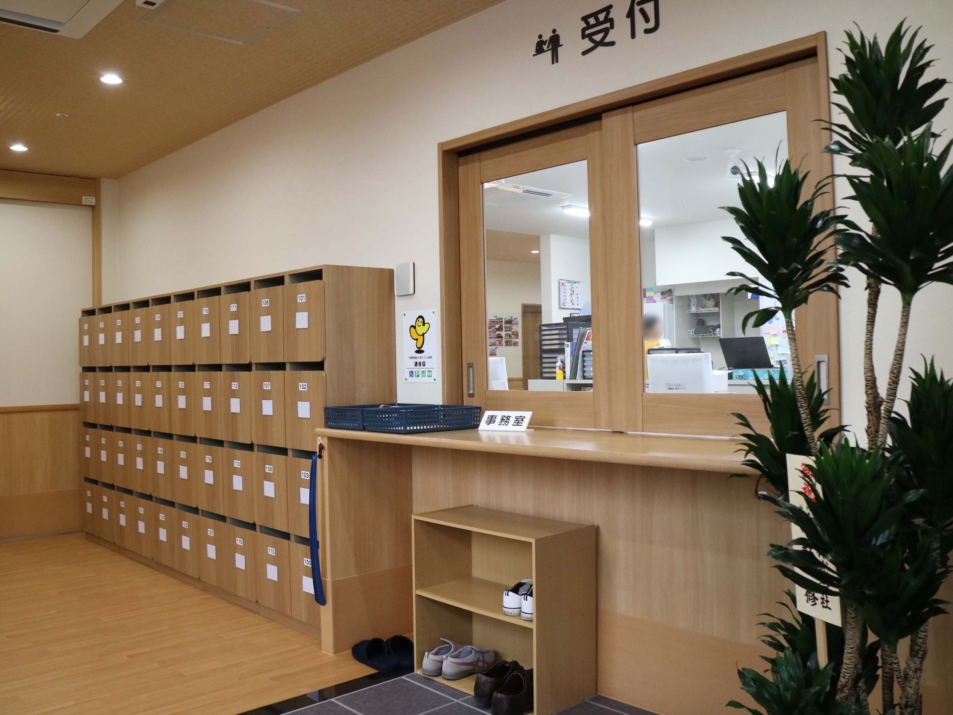 観葉植物が飾られた明るい玄関がある。右手に受付のカウンターがあり、壁沿いには下駄箱が設置されている。