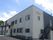 2階建ての建物は玄関には大きな屋根があり、屋外階段も付いている。ライトグレーとダークグレーの建物。