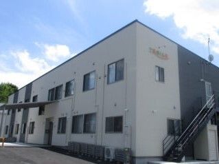 ライトグレーの2階建ての建物は玄関には大きな屋根があり、屋外階段も付き、住宅名が外壁に書かれている。