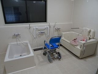 リフト付きの浴槽が右側に、左側には一人用の浴槽があり、中央にはシャワーやシャワーチェアがあり、大きな窓もある。