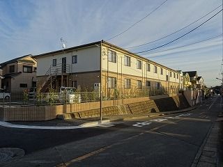 白とベージュの2階建ての建物は道路に面していて、少し高台にある。日当たりもよく、草木も植えられている。