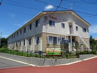 2階建ての建物はベージュと白でフロアにより外壁の色が異なり、屋外階段も付いている。