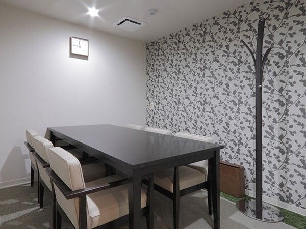 木製のテーブルセットが置かれている相談室。木の葉の模様が描かれたアクセントクロスが貼られ、木の形のハンガーラックもある。