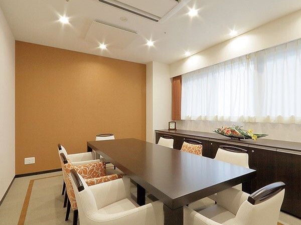 中央に置かれた長方形の大きなテーブルには白やオレンジの柄の入った椅子がセットされ、窓辺には花が飾られている。