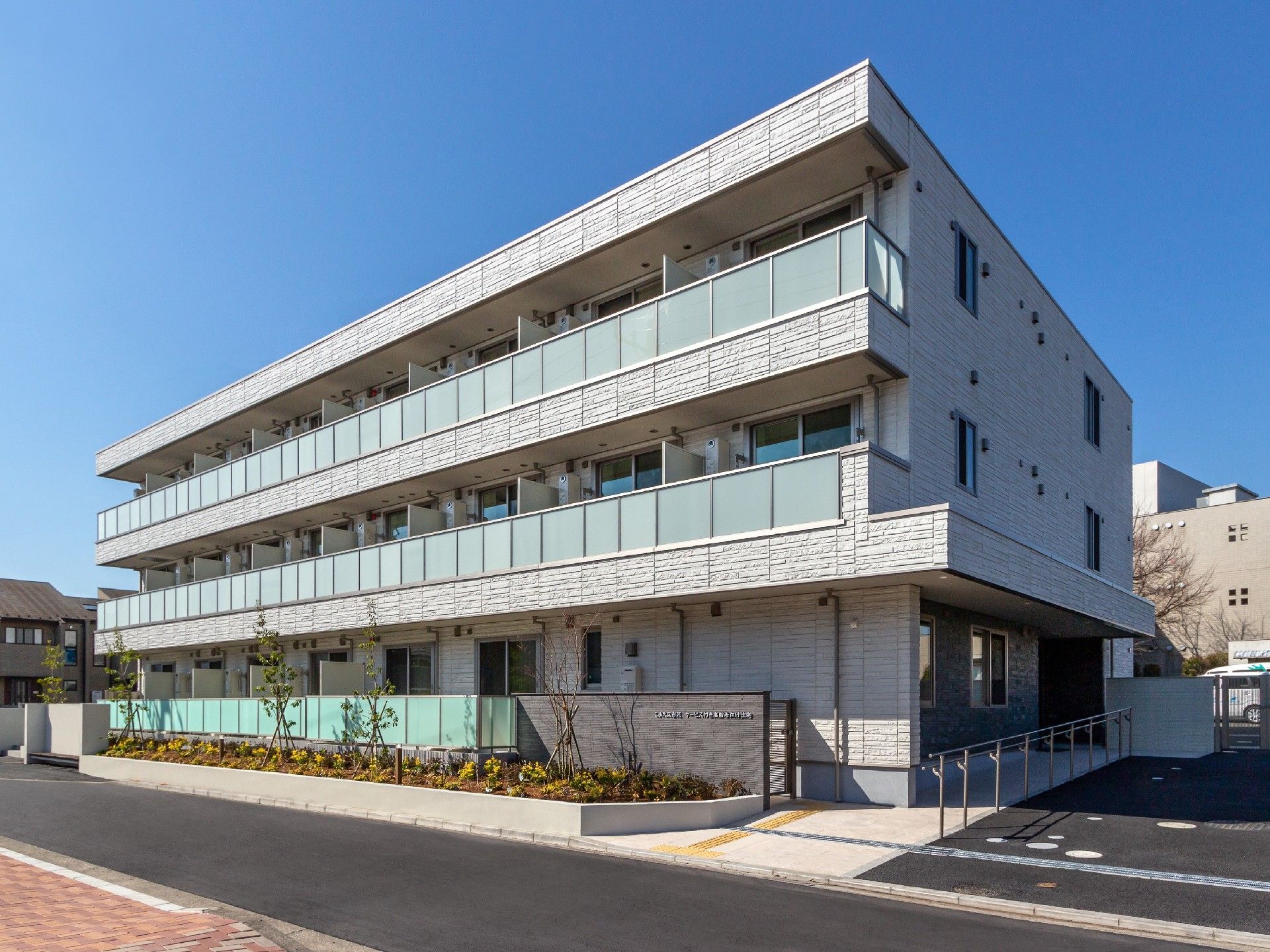 3階建ての建物はグレーを基調とした重厚感のある造り。周辺には木が植えられ、駐車場もある。