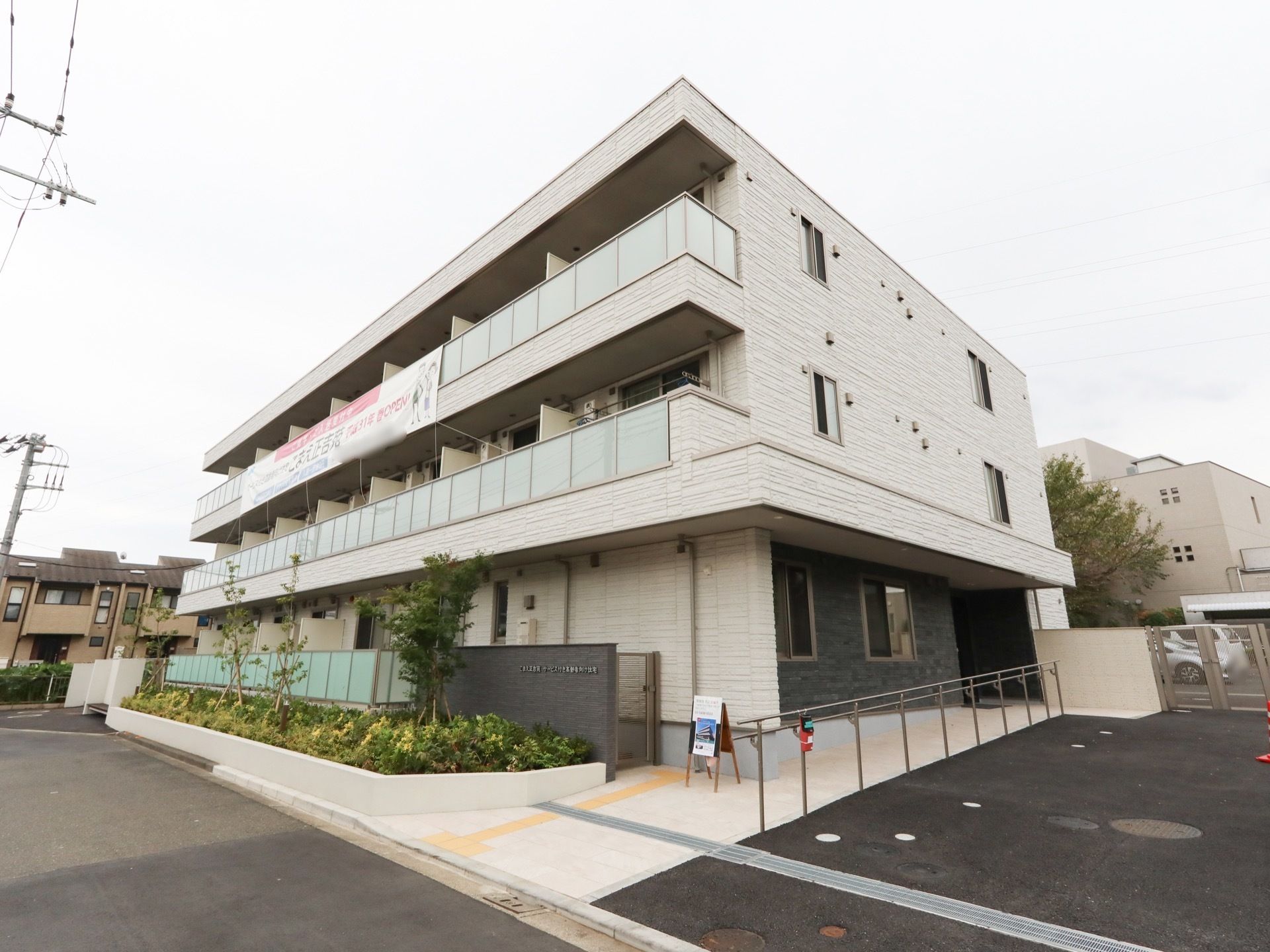 3階建の施設をスロープ側から対角線上に見た様子である。1階には植え込みが施され、2、3階にはベランダが完備されている。