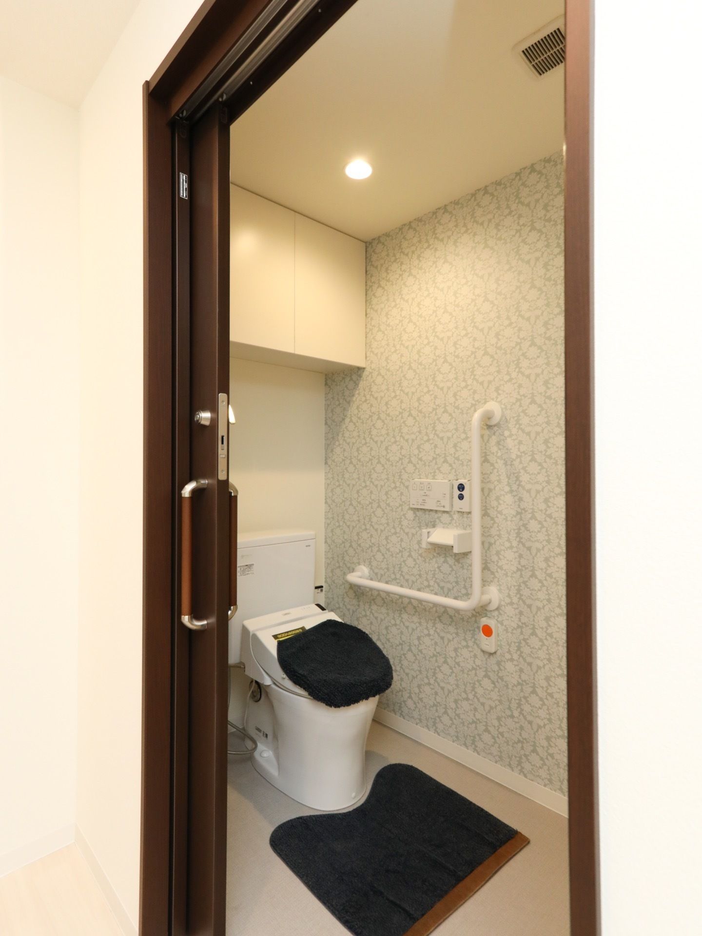 居室に完備されているトイレである。柄行きのある壁にL字型手すりと緊急呼び出しブザーがある。