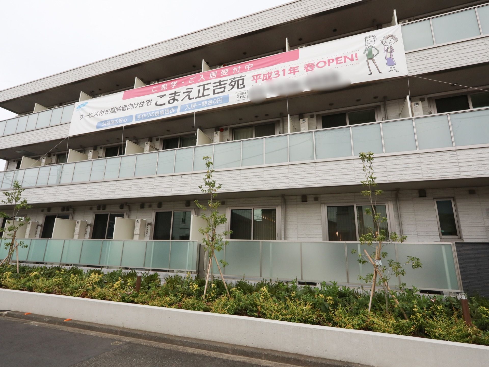 １階前面に植え込みが完備された３階建の施設である。３階ベランダ部分に施設紹介の垂れ幕が吊るされている。