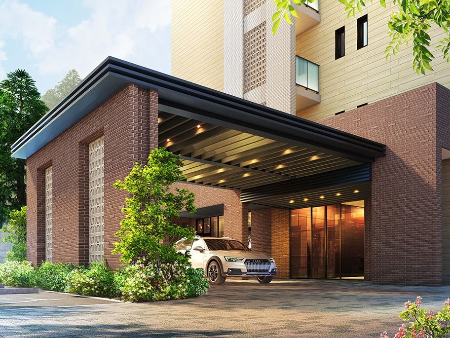 レンガ調の外壁がおしゃれな車寄せが付いたベージュ系の建物。敷地内にはたくさんの木も植えられている。