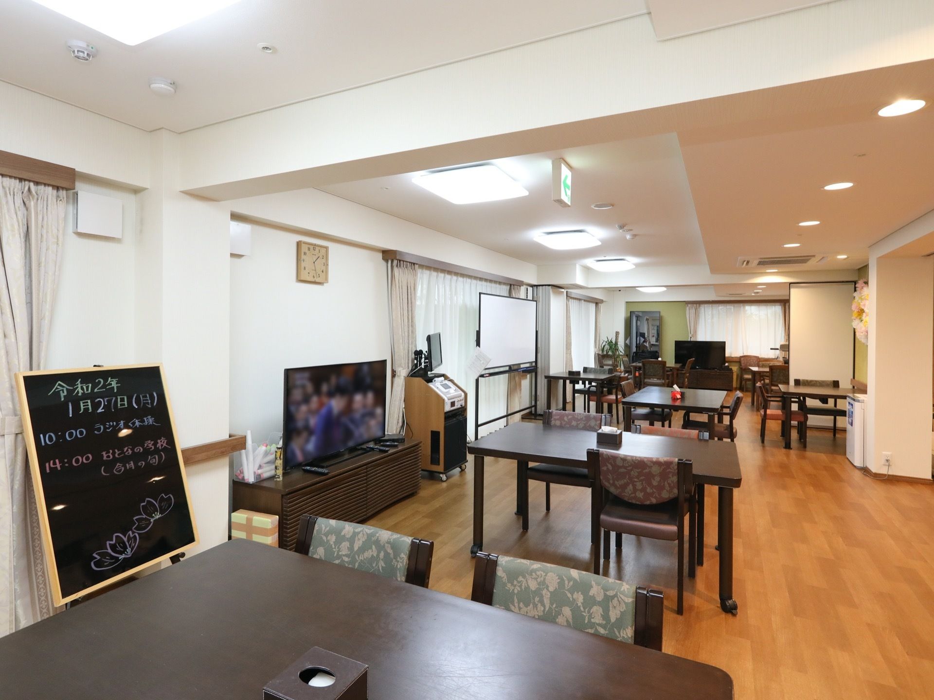 食堂は窓側に寄せて、テレビやホワイトボードなどの家具を配置している。黒板には1日の予定を記載して掲示してある。