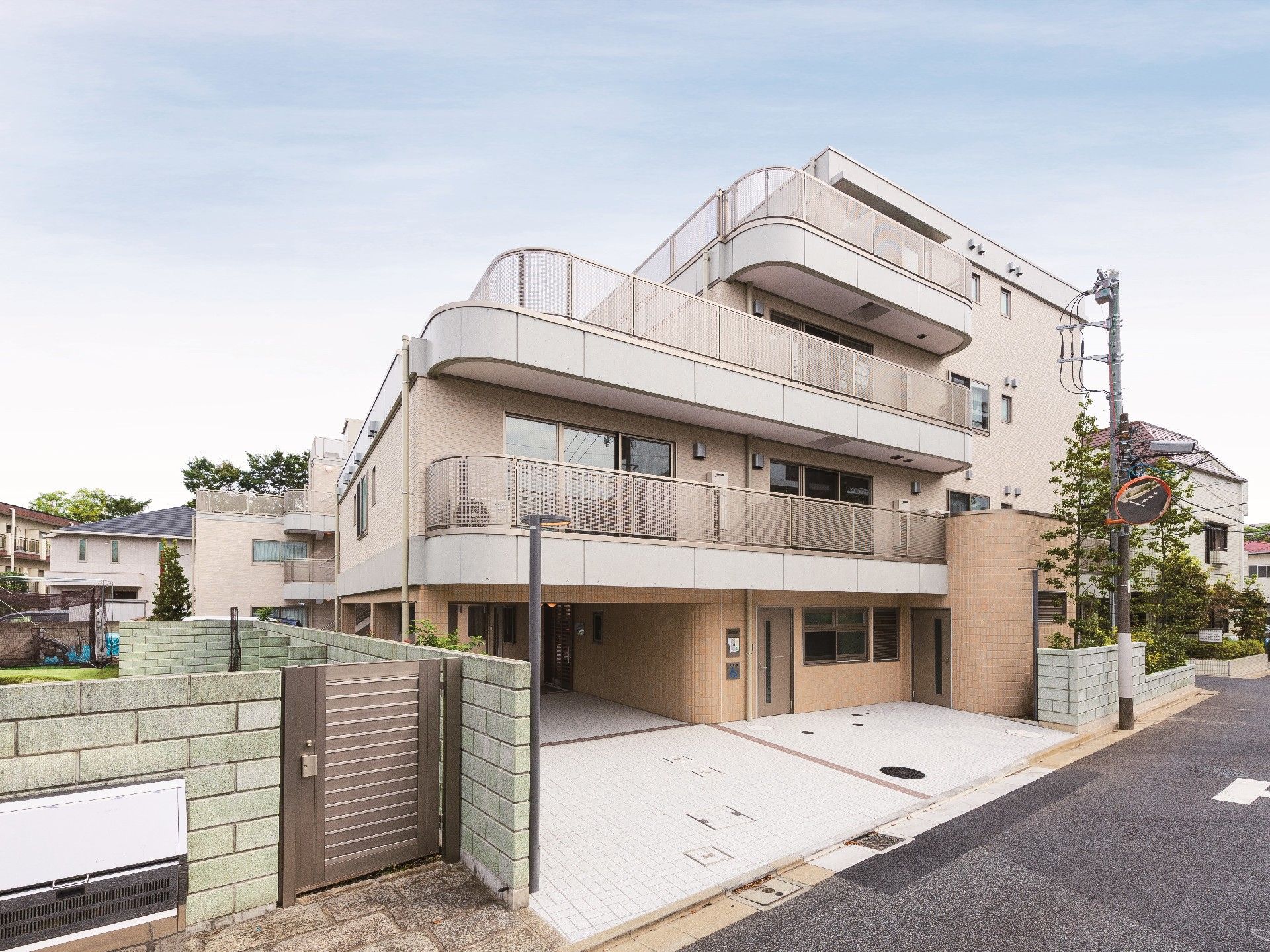 住宅地にある建物はベージュ系で周辺の景観によくなじんでいる。4階建てでベランダや駐車場がある。