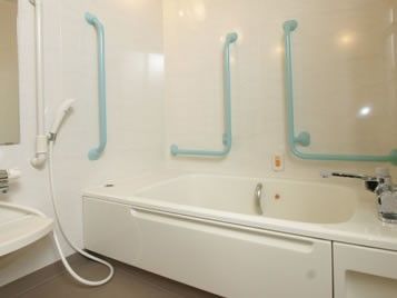 水色の手すりが付いた白を基調とした浴室。呼び出しボタンも浴槽のそばについている。