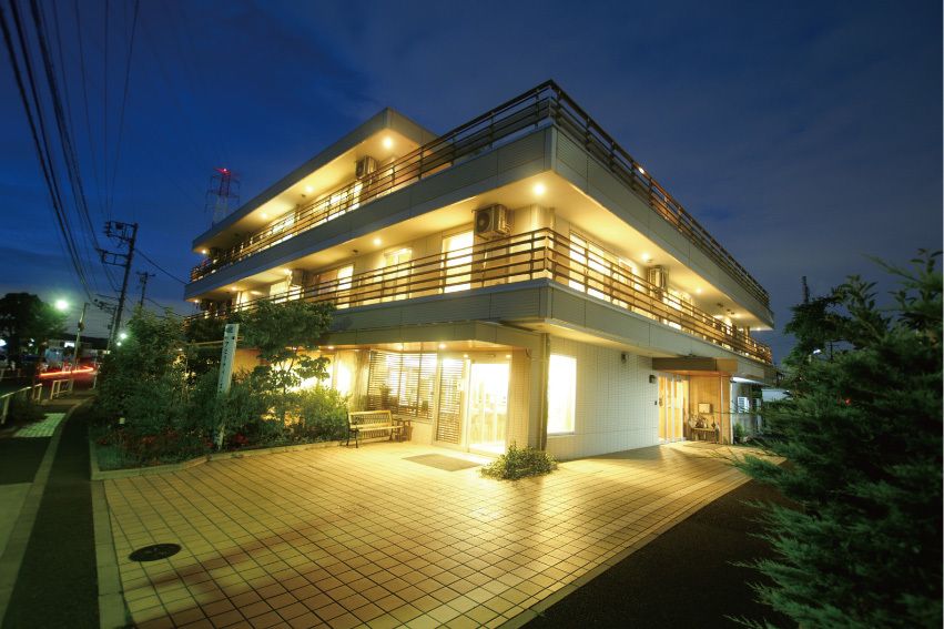 たくさんの窓が付いた３階建ての建物にはベランダもある。日が暮れて窓からは光が漏れている。