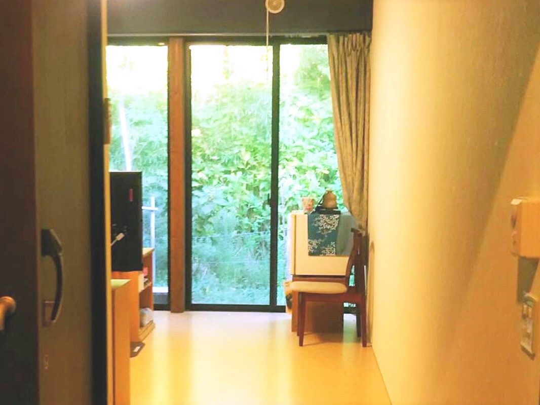 大きな窓にはカーテンが付いているが、カーテンは開けられ、外の緑あふれる風景を見ることができる。窓のそばにはいすも置かれている。