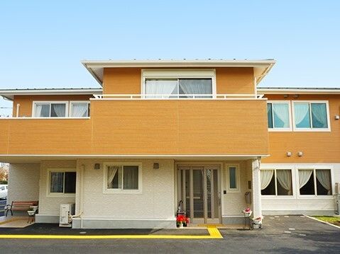 2階建ての建物の2階部分にはベランダが付き、玄関には点字ブロックや花が植えられたプランターがある。
