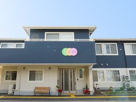 2階建ての建物の2階部分にはベランダが付き、玄関周辺には点字ブロックがある。玄関脇にはベンチが置かれ、駐車スペースもある。